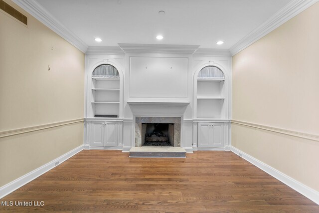 unfurnished living room featuring dark wood-type flooring, crown molding, a premium fireplace, and built in shelves