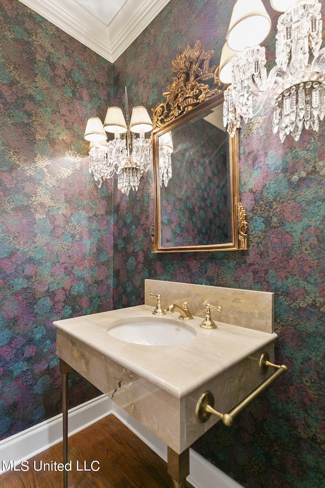 bathroom with wood finished floors, a sink, baseboards, a chandelier, and ornamental molding