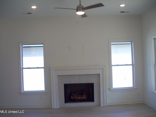 unfurnished living room featuring light wood-type flooring, a tile fireplace, and ceiling fan