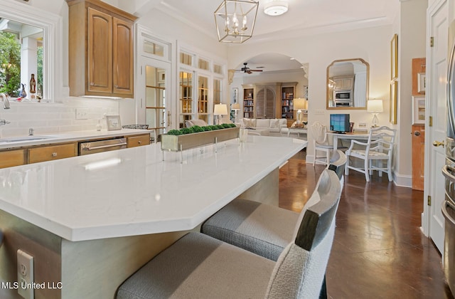 kitchen with stainless steel appliances, ornamental molding, sink, pendant lighting, and ceiling fan with notable chandelier