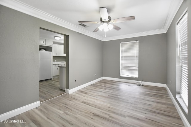 spare room featuring visible vents, ornamental molding, a ceiling fan, light wood-type flooring, and baseboards