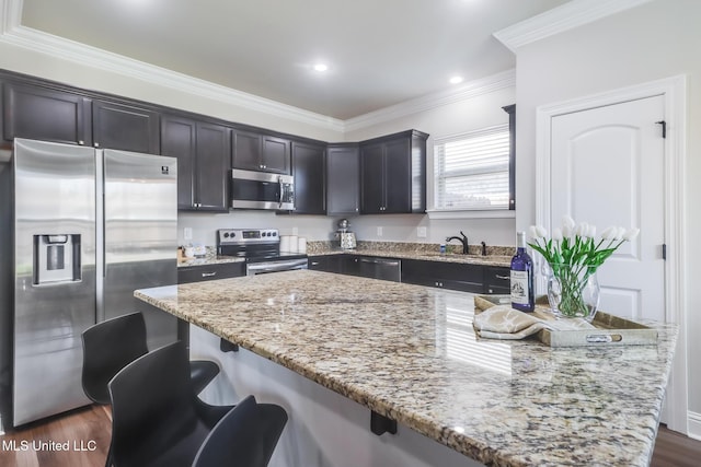 kitchen featuring appliances with stainless steel finishes, a center island, light stone counters, ornamental molding, and a breakfast bar