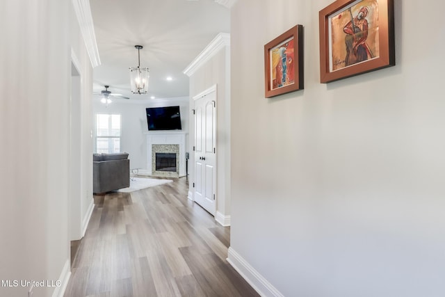 hallway with baseboards, ornamental molding, wood finished floors, and a notable chandelier