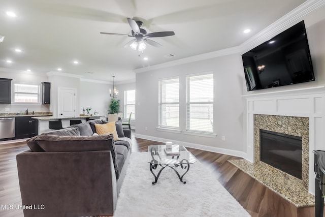 living room with dark wood-style flooring, crown molding, ceiling fan with notable chandelier, recessed lighting, and a premium fireplace