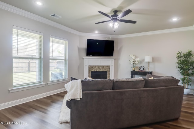 living room featuring a ceiling fan, visible vents, crown molding, a fireplace, and dark wood finished floors