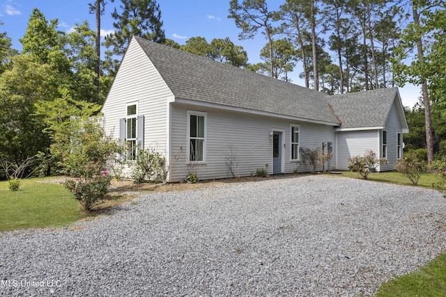 view of front of home featuring roof with shingles, a front lawn, and gravel driveway