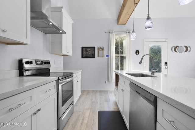 kitchen with pendant lighting, light wood-type flooring, a sink, stainless steel appliances, and wall chimney exhaust hood