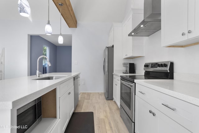 kitchen with wall chimney range hood, white cabinetry, a sink, light wood-style flooring, and stainless steel appliances