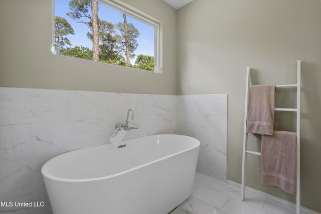 full bathroom with a wainscoted wall, marble finish floor, a freestanding bath, and tile walls