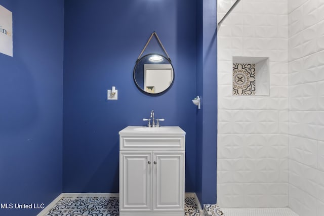 bathroom featuring baseboards, tiled shower, tile patterned floors, and vanity