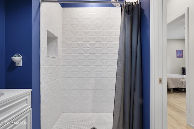 ensuite bathroom with ensuite bathroom, wood finished floors, a tile shower, and vanity