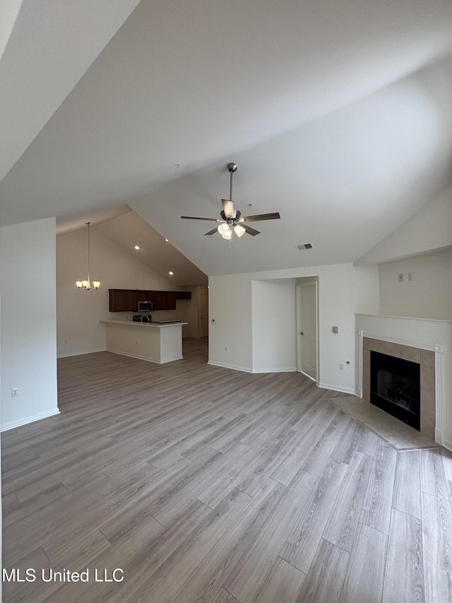 8911 Oak Branch Ln, Olive Branch, MS 38654 - unfurnished living room featuring vaulted ceiling, a tiled fireplace, light wood-style flooring, a chandelier, and ceiling fan