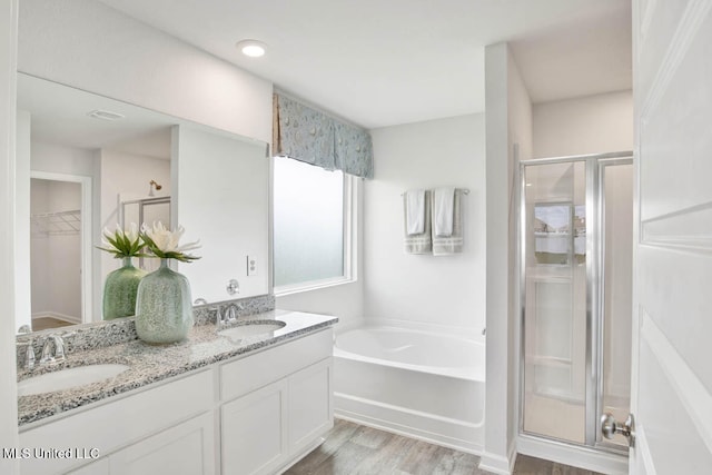 bathroom with a shower stall, wood finished floors, a garden tub, a walk in closet, and double vanity