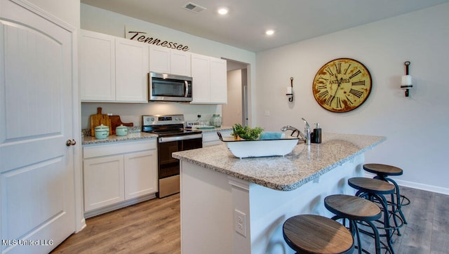kitchen with appliances with stainless steel finishes, light wood finished floors, a breakfast bar area, white cabinets, and recessed lighting