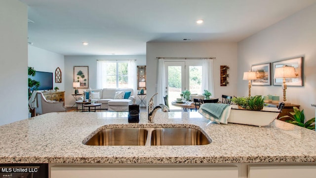 kitchen featuring a sink, open floor plan, light stone countertops, recessed lighting, and a center island with sink