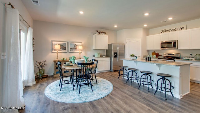 kitchen featuring appliances with stainless steel finishes, light wood-style flooring, white cabinetry, a breakfast bar area, and light stone countertops