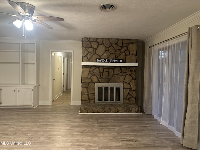 unfurnished living room with a stone fireplace, ornamental molding, ceiling fan, a textured ceiling, and light wood-type flooring