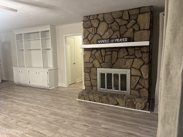 unfurnished living room featuring crown molding, a stone fireplace, light hardwood / wood-style floors, and a textured ceiling