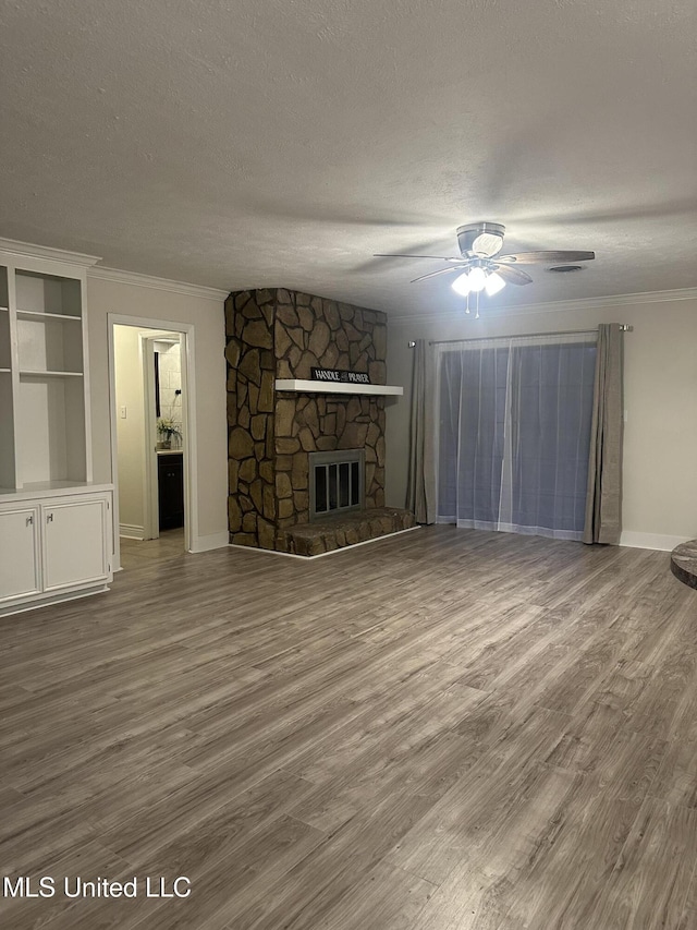 unfurnished living room featuring a stone fireplace, ornamental molding, a textured ceiling, and hardwood / wood-style flooring