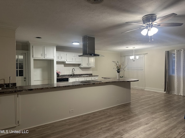 kitchen with island range hood, dark stone countertops, white cabinets, kitchen peninsula, and crown molding