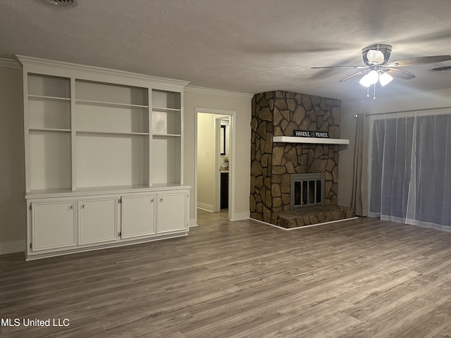 unfurnished living room with ceiling fan, ornamental molding, light hardwood / wood-style floors, a textured ceiling, and a stone fireplace