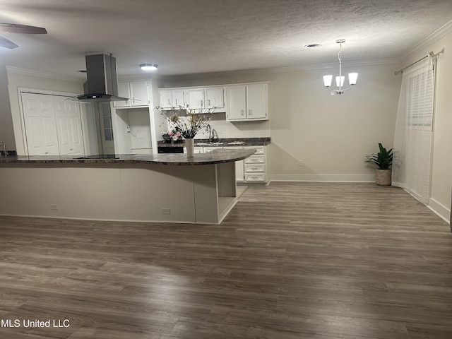 kitchen featuring hanging light fixtures, kitchen peninsula, island exhaust hood, dark stone counters, and white cabinets