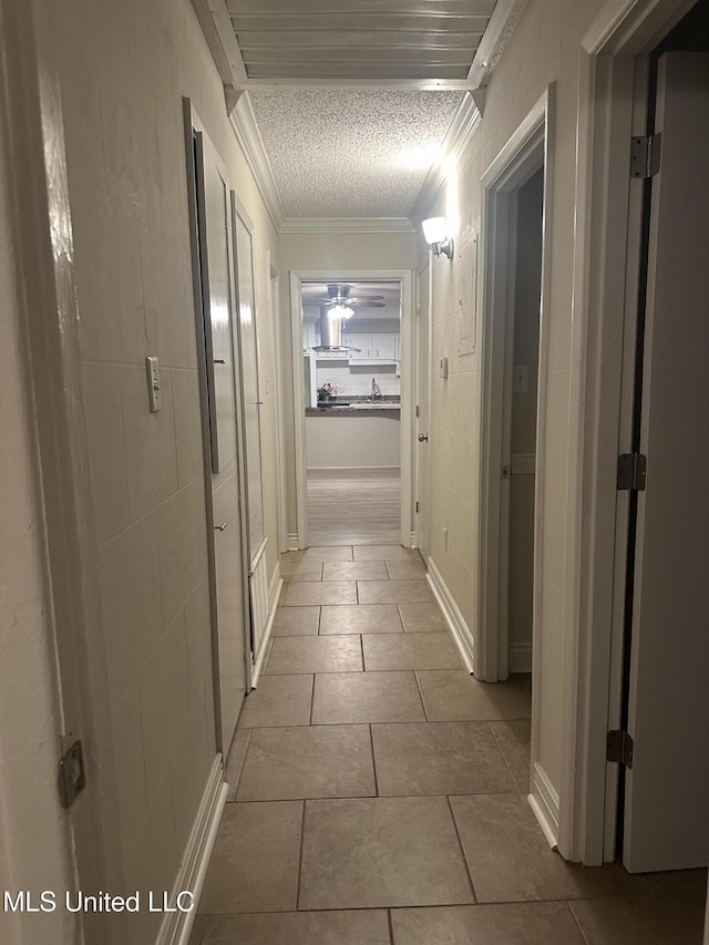 corridor with crown molding, a textured ceiling, and light tile patterned floors