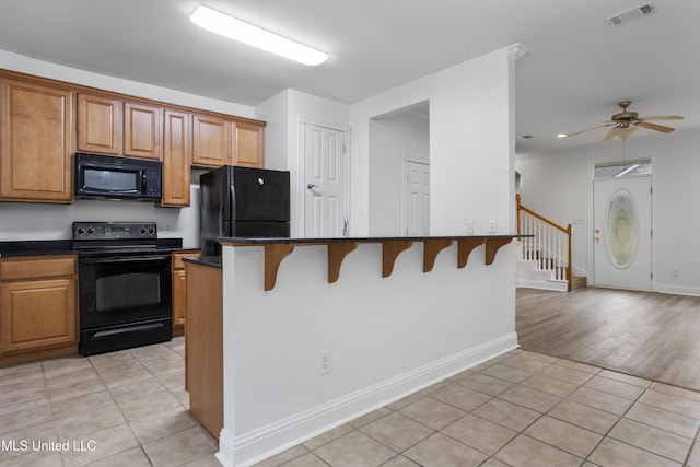 kitchen with a breakfast bar, a center island, light tile patterned floors, and black appliances