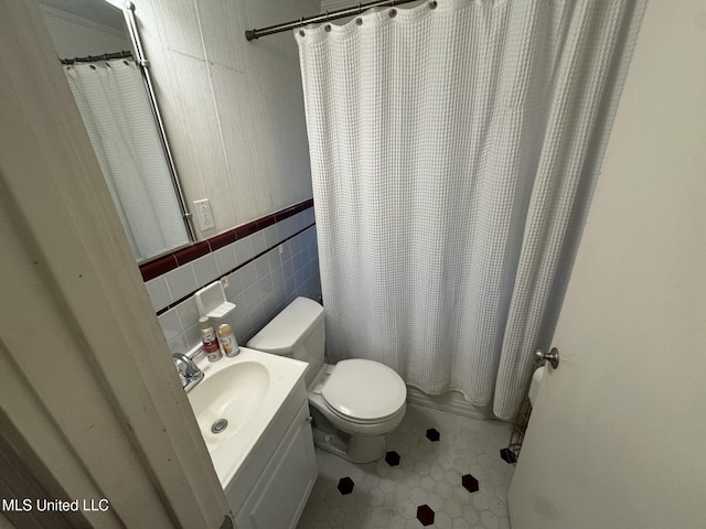 full bathroom featuring tile patterned floors, toilet, tile walls, wainscoting, and vanity