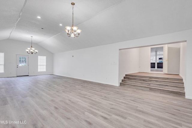 unfurnished living room with a chandelier, a textured ceiling, light hardwood / wood-style floors, and lofted ceiling