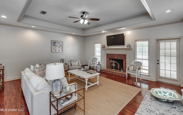 221 Boxwood Cir, Brandon, MS 39047 - living area with a tray ceiling, a ceiling fan, ornamental molding, a brick fireplace, and dark wood-style flooring
