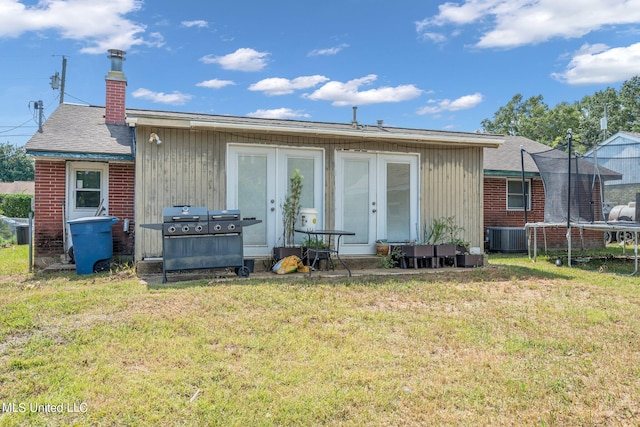 back of property with french doors, a trampoline, and a lawn