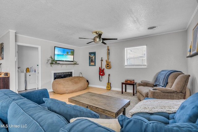 living room featuring washing machine and dryer, a textured ceiling, a tile fireplace, ceiling fan, and crown molding