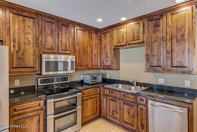 kitchen featuring dark stone counters, sink, light tile patterned floors, and stainless steel appliances