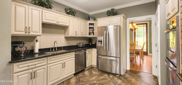 kitchen featuring ornamental molding, stainless steel appliances, sink, a notable chandelier, and dark stone countertops