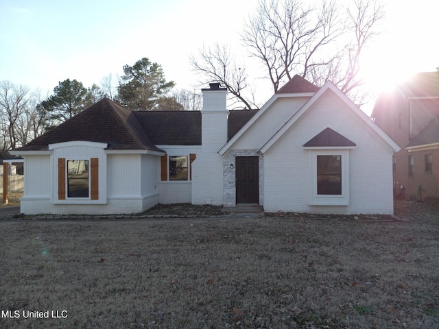 view of front facade with a shingled roof, a chimney, a front lawn, and brick siding