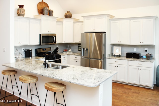 kitchen featuring light wood finished floors, a peninsula, appliances with stainless steel finishes, and white cabinets