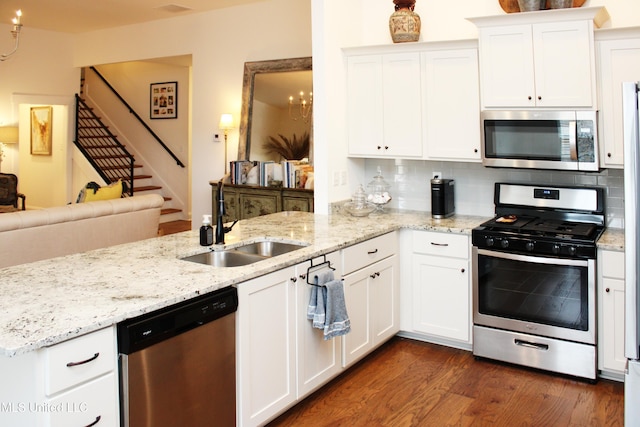 kitchen featuring stainless steel appliances, decorative backsplash, dark wood-type flooring, a sink, and a peninsula