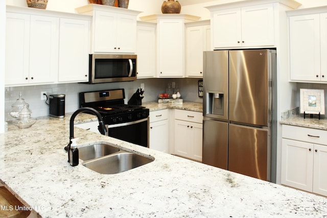 kitchen with stainless steel appliances, a sink, white cabinets, decorative backsplash, and light stone countertops