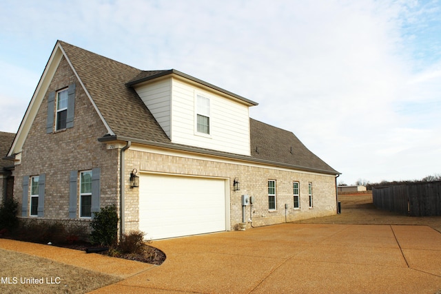 view of side of property featuring concrete driveway, brick siding, fence, and roof with shingles