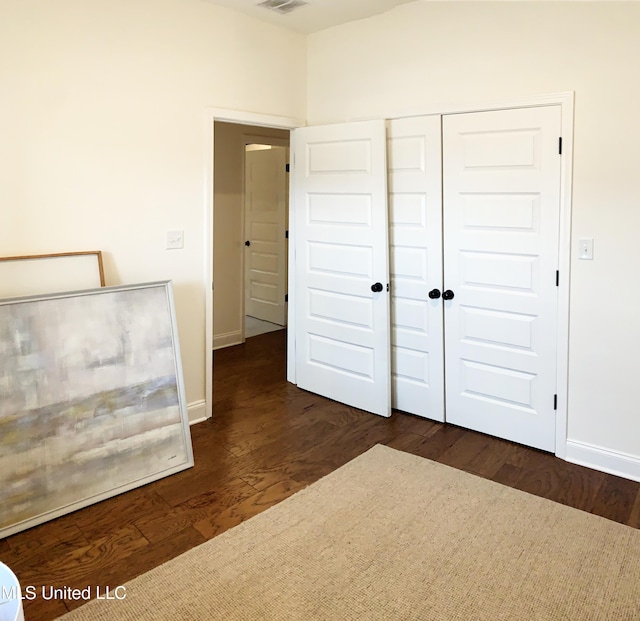 unfurnished bedroom with dark wood-type flooring, a closet, visible vents, and baseboards