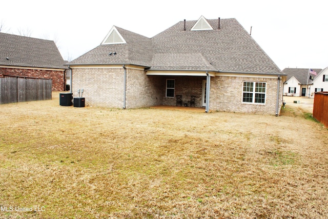 back of property featuring brick siding, fence, a lawn, and roof with shingles