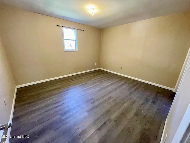 spare room featuring baseboards and dark wood-type flooring