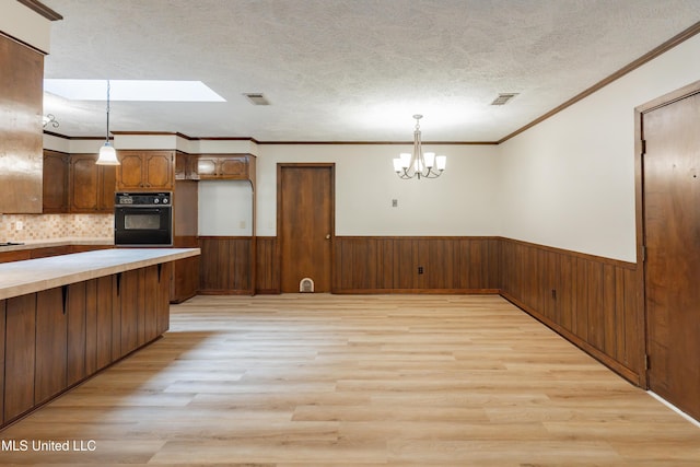 504 Hampton St, Clinton, MS 39056 - kitchen featuring black oven, light wood-style floors, a chandelier, wainscoting, and light countertops