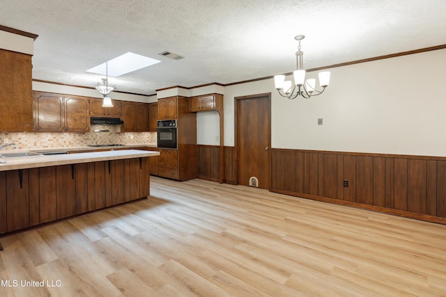 504 Hampton St, Clinton, MS 39056 - kitchen featuring black oven, a chandelier, light wood finished floors, under cabinet range hood, and a wainscoted wall