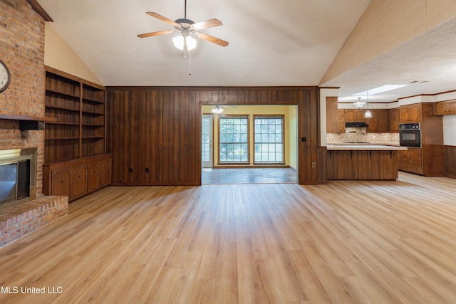 504 Hampton St, Clinton, MS 39056 - unfurnished living room featuring lofted ceiling, light wood-style flooring, ceiling fan, a fireplace, and wooden walls