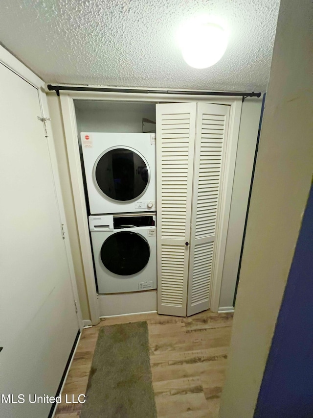 laundry room featuring stacked washer / drying machine, light wood-type flooring, and a textured ceiling