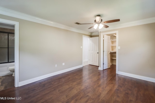 unfurnished bedroom with ensuite bathroom, a spacious closet, crown molding, dark wood-type flooring, and a closet