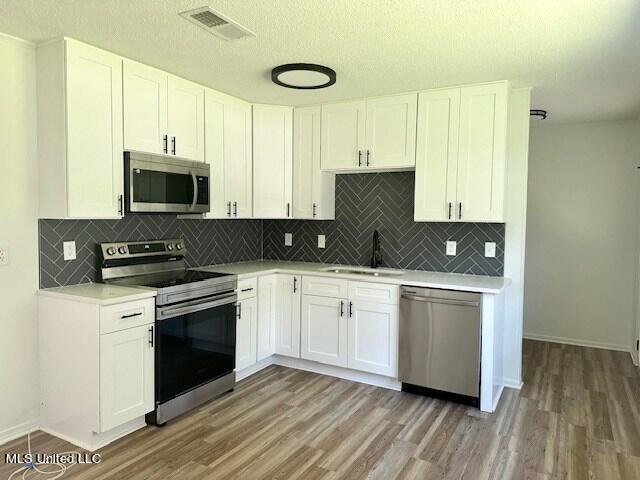 kitchen with white cabinetry, light hardwood / wood-style floors, appliances with stainless steel finishes, and decorative backsplash