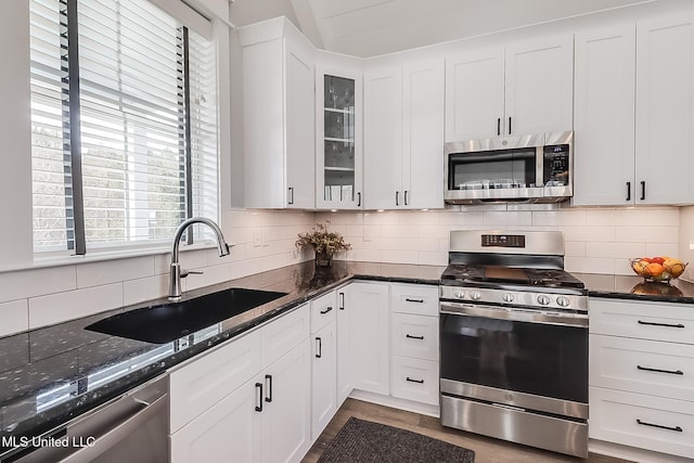 kitchen featuring appliances with stainless steel finishes, white cabinetry, sink, dark stone countertops, and backsplash